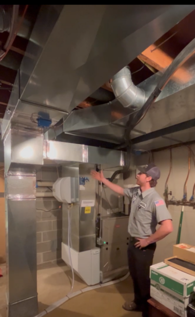 HVAC technician from Streitz Heating & Cooling inspecting furnace and ductwork system in a Minnesota home basement.